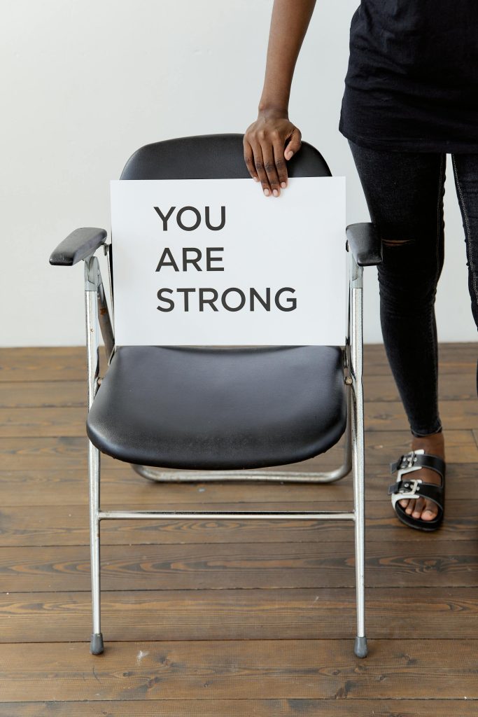 A person holds a card with 'You Are Strong' on a chair, symbolizing support and empowerment.