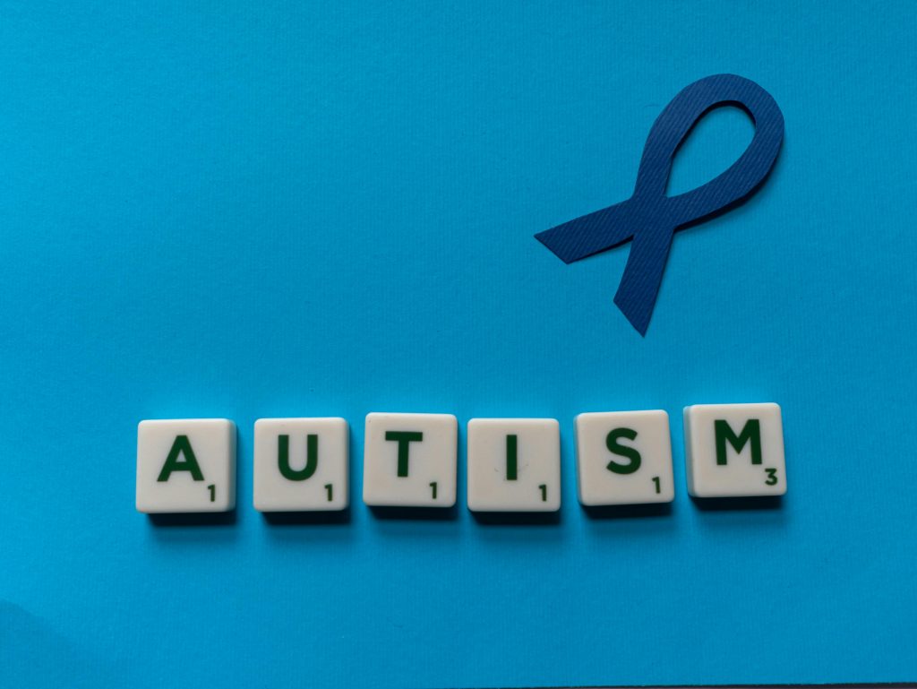 Courses Flat lay of scrabble tiles spelling autism with a blue ribbon on a blue background.